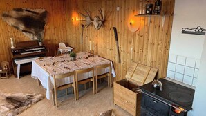 Una stanza rustica con pareti in legno, un tavolo da pranzo per quattro persone, un pianoforte, un camino e tappeti in pelliccia sul pavimento.
