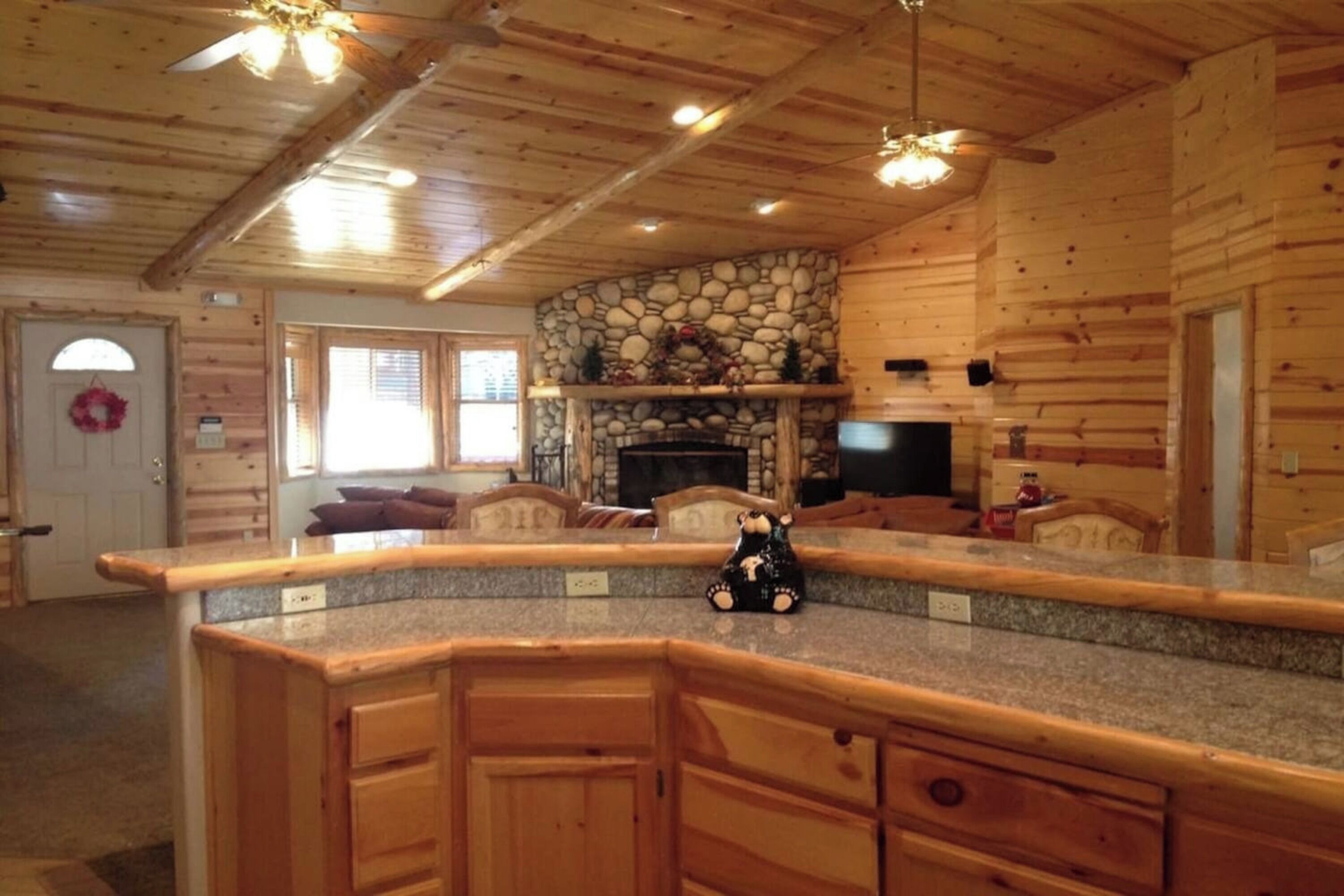 A log cabin interior with a stone fireplace, wooden cabinets, and a ceiling fan.