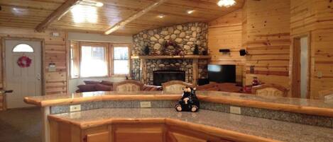 A log cabin interior with a stone fireplace, wooden cabinets, and a ceiling fan.
