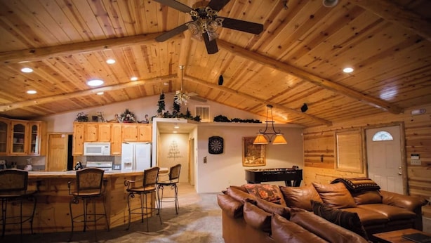 A spacious living area with a wooden ceiling, a leather sofa, a dining area with bar stools, and a kitchen in the background. - Luxury w Spa Foosball - DeCarlo House (Big Bear Lake)