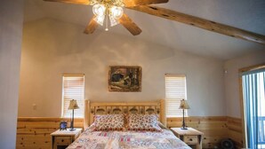 A bedroom with a wooden bed, two bedside tables, a ceiling fan, and a painting on the wall. - Luxury w Spa Foosball - DeCarlo House (Big Bear Lake)
