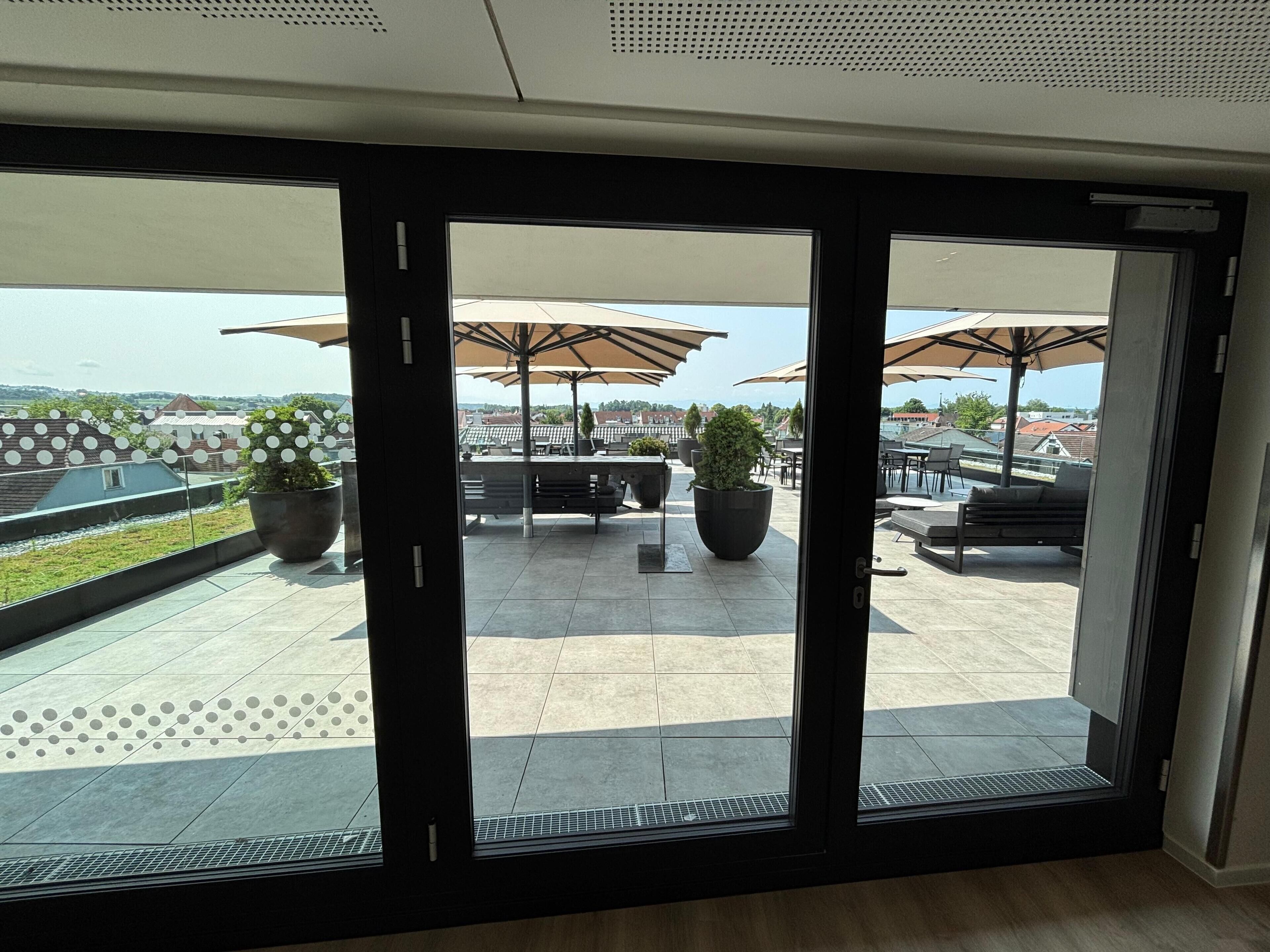 Un patio moderno al aire libre con mobiliario y sombrillas, vista del paisaje urbano y plantas en macetas.
