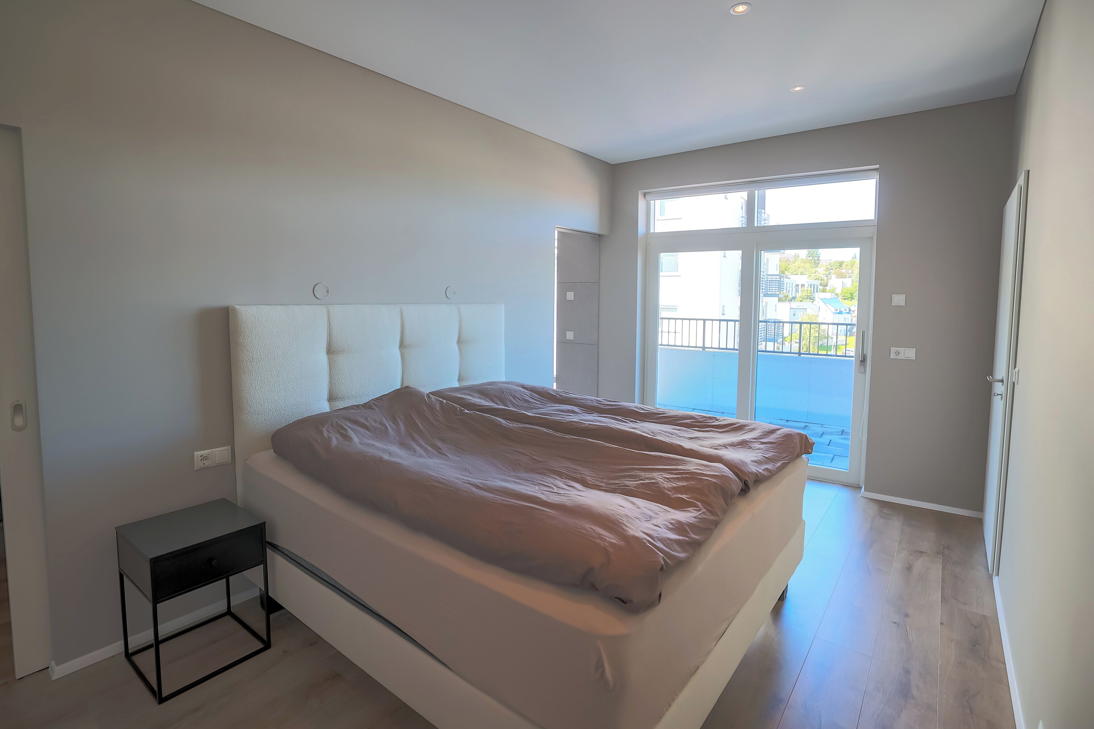 Une chambre à coucher comprenant un lit, une table de chevet et une porte-fenêtre coulissante donnant sur un balcon.