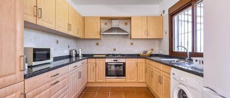A compact kitchen with wooden cabinets, a built-in oven, a microwave, and a washing machine.
