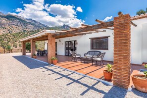 A patio with outdoor furniture and potted plants, a white building with a tiled roof, and a mountainous backdrop. - Casa del Molino, a beautiful Villa in the mountains of Canillas de Aceituno (CANILLAS DE ACEITUNO)