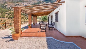 Un patio cubierto con un pilar de ladrillo, mobiliario exterior y vistas a un paisaje montañoso.