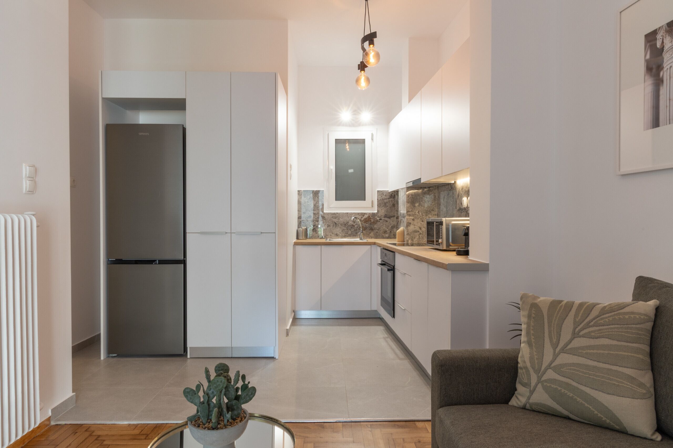 A compact kitchen with a built-in refrigerator, a dining area with a table and chairs, and a living room with a sofa and a plant.