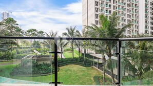 A high-rise building with a balcony overlooking a well-maintained garden with palm trees and a pathway. - Belia by Kozystay - BSD (Pagedangan)
