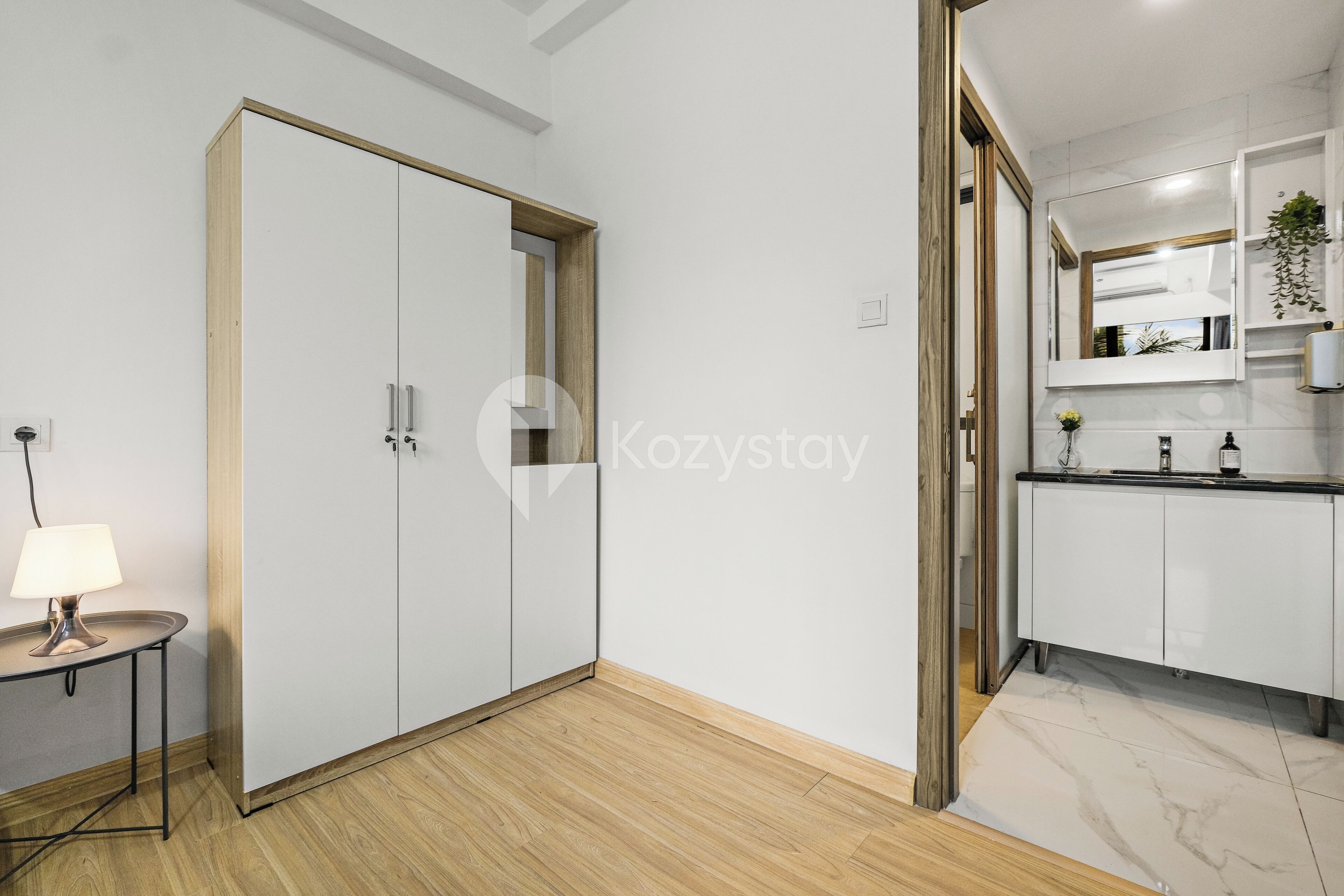 A modern apartment with a wardrobe, a small table with a lamp, and a kitchen area with cabinets and a countertop.