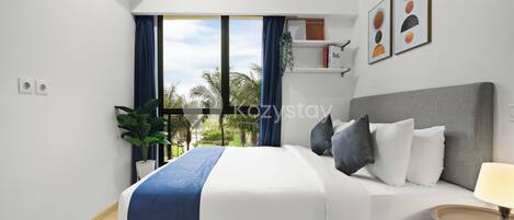 A modern hotel room with a bed, a bedside table, an air conditioning unit, a window with curtains, and a view of palm trees.