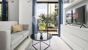 A modern living room with a grey sofa, a black coffee table, and a TV on a white cabinet. - Belia by Kozystay - BSD (Pagedangan)