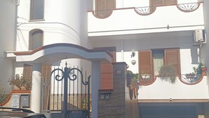 A two-story building with a white facade, a balcony with a wrought iron gate, and a small garden area with potted plants. - Home  Peppe (Manduria)