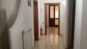 A hallway with tiled flooring, white walls, and a radiator. There is a door with a window at the end of the hallway. - Home  Peppe (Manduria)