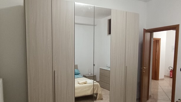 A bedroom with a large wardrobe, a bed with a blue pillow, and a small bedside table. - Home  Peppe (Manduria)