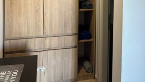 Ein Zimmer mit einem Holzschrank, einer weißen Deckenleuchte und einer Tür zu einem weiteren Raum.