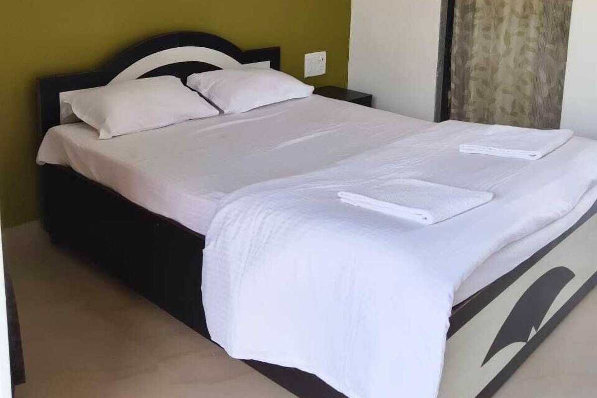 A single bed with white bedding in a room with green walls and a window with patterned curtains.