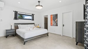 A modern bedroom with a large bed, bedside tables, a ceiling light, a window with curtains, and a door. - 3BR Villa in Aruba · Private Pool · Prime Location (Noord)