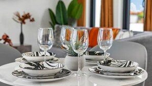 A dining table set with black and white striped plates, clear glasses, and a white vase with green leaves. - 3BR Villa in Aruba · Private Pool · Prime Location (Noord)