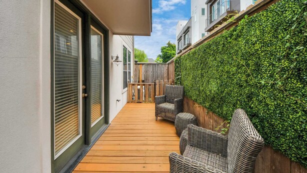 A wooden deck with wicker furniture, a wooden fence, and a green hedge wall. - Luxurious Three-Story Townhome in Houston (Houston)