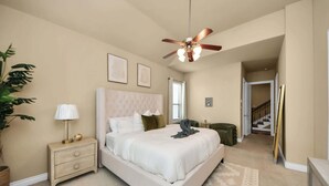A bedroom with a large bed, a nightstand, a ceiling fan, a window, and a staircase leading to another level. - Luxurious Three-Story Townhome in Houston (Houston)