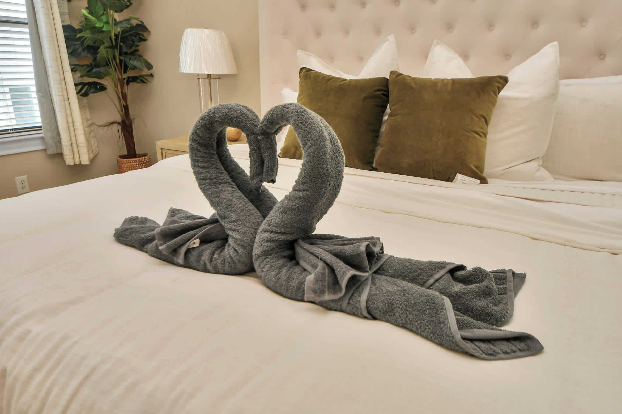 Una cama bien hecha con una toalla dispuesta en forma de corazón sobre la colcha.