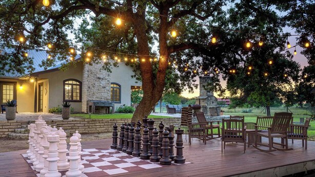 A chessboard set up on a wooden deck with chairs and string lights. - Birdsong - Hot Tub, Lawn Games, Close to Wineries (Fredericksburg)