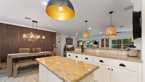 Una cocina moderna con encimeras de granito, una mesa de comedor de madera, iluminación colgante y una isla grande.