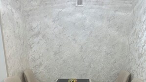 Kulhuone, jossa on marmoriseinä, pieni pöytä ja kaksi tuolia sekä kalanruotokuviollinen lattia.