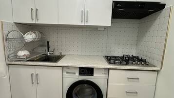 Cocina compacta con alacenas blancas, lavadora integrada, estufa a gas y salpicadero de azulejos.