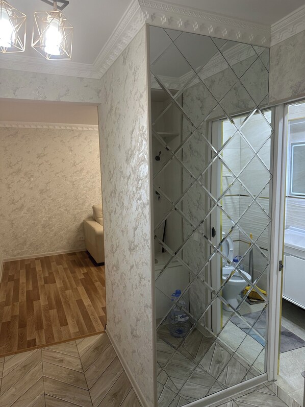 A room with a herringbone patterned wooden floor, a white textured wall, and a glass partition with a diamond pattern.
