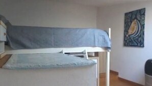 Een kamer met een stapelbed, een klein tafeltje, een stoel, een schilderij aan de muur en een afvalbak.