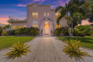 A two-story house with a central entrance, a covered porch, and a well-maintained garden with palm trees and shrubs.