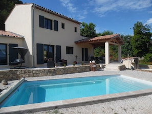 A two-story house with a swimming pool, outdoor seating, and a pergola.