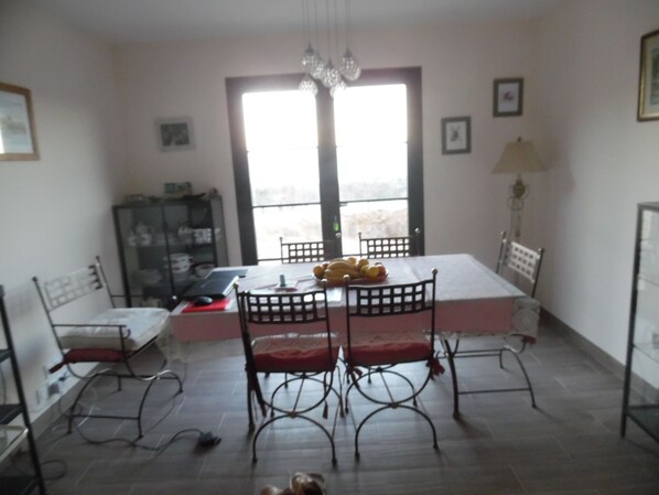 A dining area with a table and chairs, a bookshelf, and a view through a door.