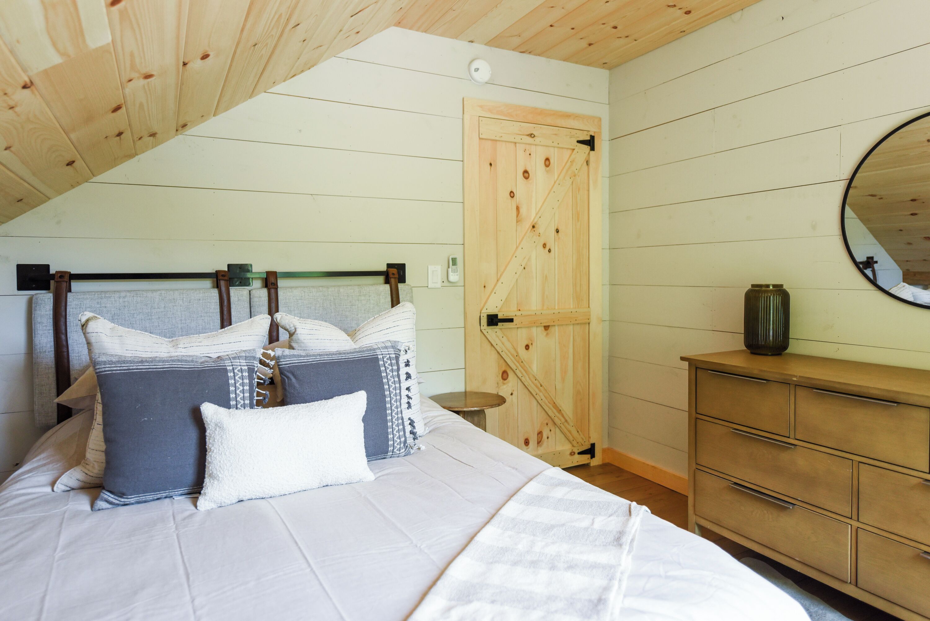 A bedroom with a bed, pillows, a dresser, a mirror, and a wooden door.