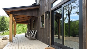 Une terrasse en bois avec des chaises, un espace couvert et une grande porte vitrée donnant sur la terrasse.