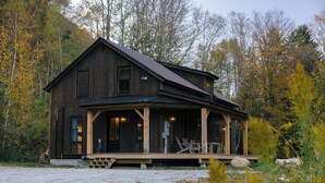 Une cabane en bois rustique, dotée d’un porche et entourée du feuillage automnal.