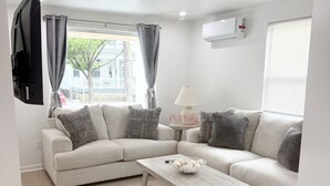 A living room with a sectional sofa, a coffee table, a TV mounted on the wall, and a window with curtains. - Shore Thing Wildwood (Wildwood)