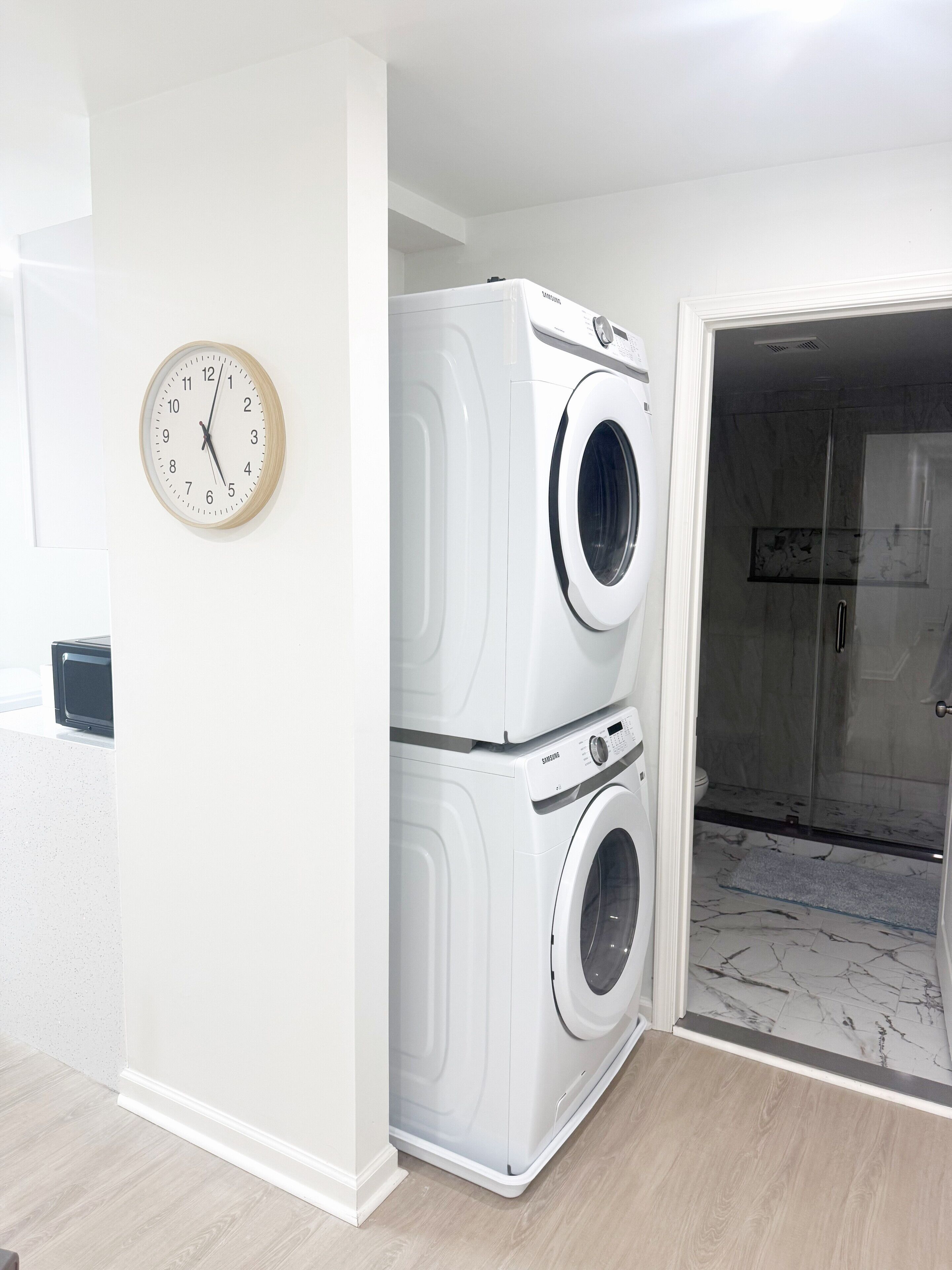 A laundry room with two stacked washing machines and a clock on the wall.