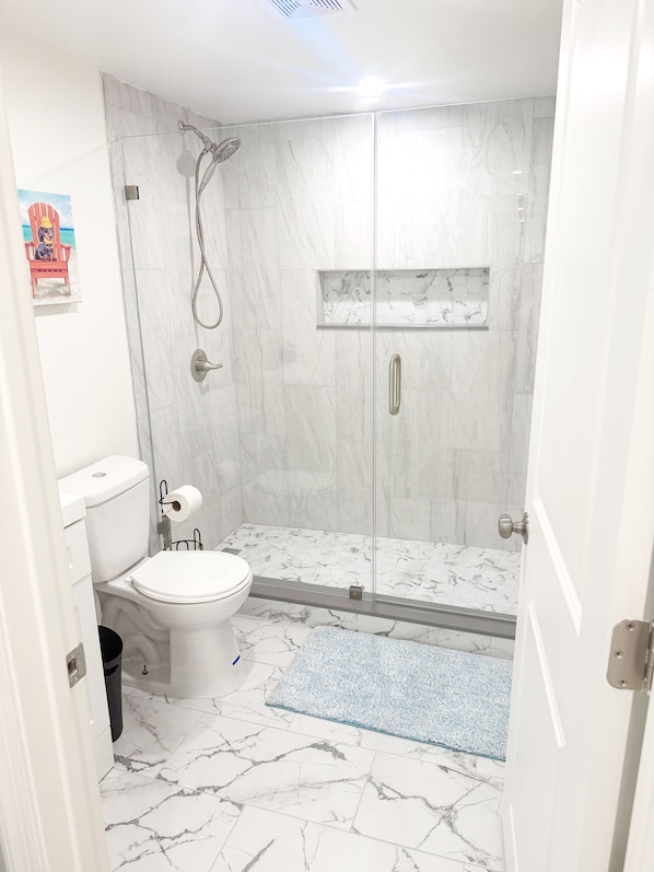 Un baño moderno con ducha envuelta en vidrio, inodoro y suelo con diseño de mármol.