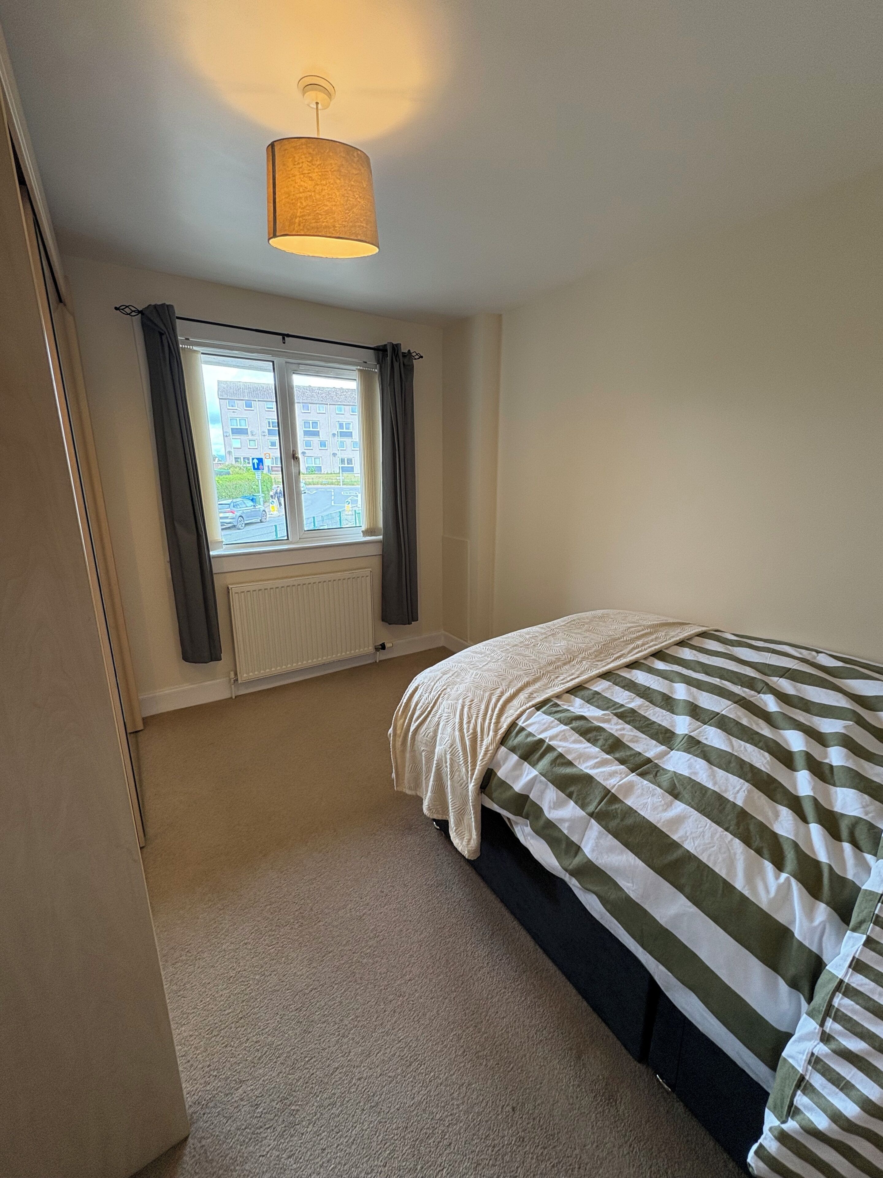 A bedroom with a bed, a window with curtains, a radiator, and a hanging light fixture.