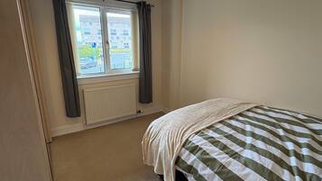 A bedroom with a bed, a window with curtains, a radiator, and a hanging light fixture.