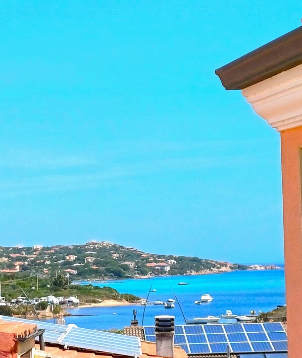 A coastal view with solar panels on rooftops, a clear blue sea, and a hilly landscape in the background. - Affittimoderni La Maddalena - MADA43 (La Maddalena)