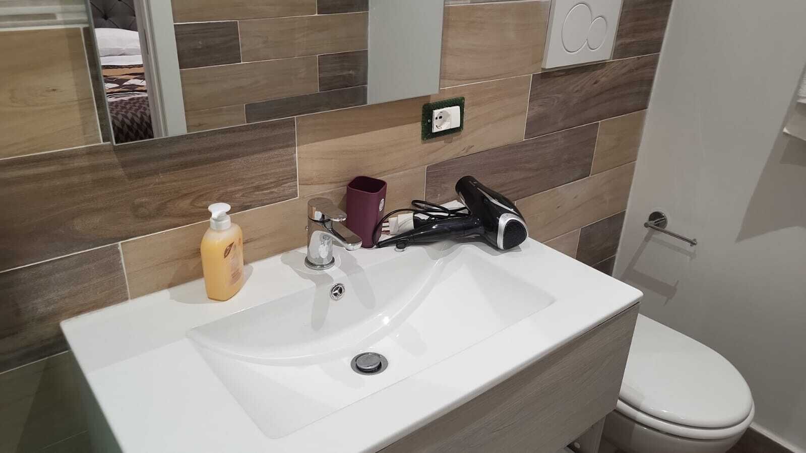 Een badkamer met een wit wastafel, een spiegel, een haardroger en een toilet.