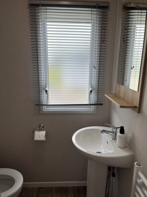 Ein Badezimmer mit Toilette, Waschbecken und einem Fenster mit Jalousien.