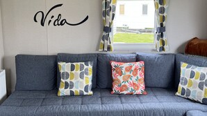 En grå modulsofa med mønstrede puder, en væg med 'Pura Vida' skrevet på den, og et vindue med gardiner.