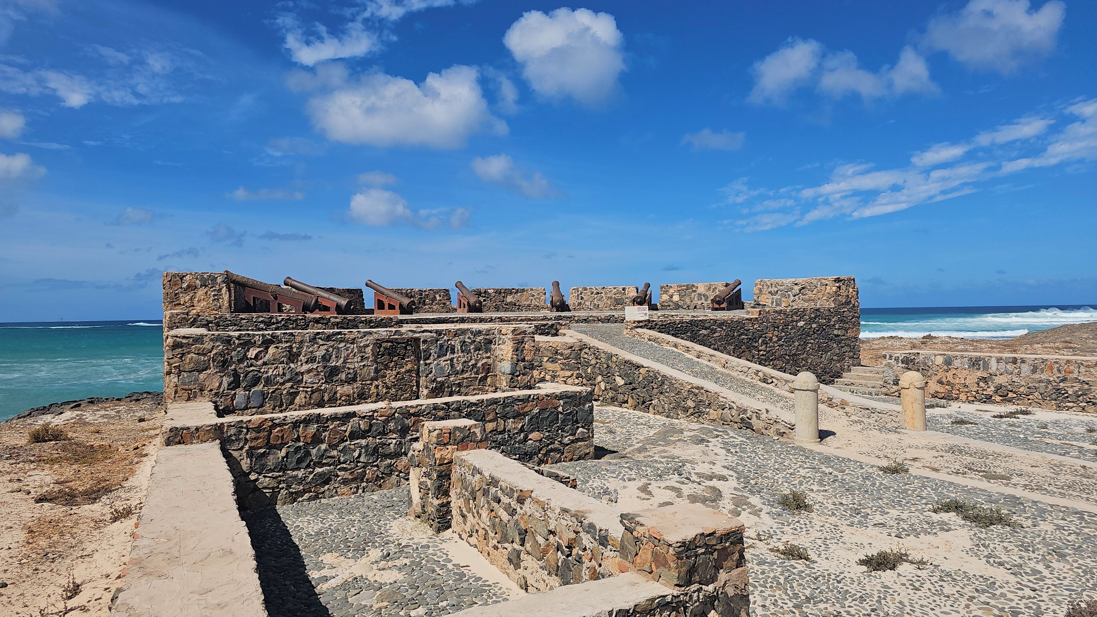 Een stenen fortificatie met kanonnen, een stenen trap en uitzicht op de kust.
