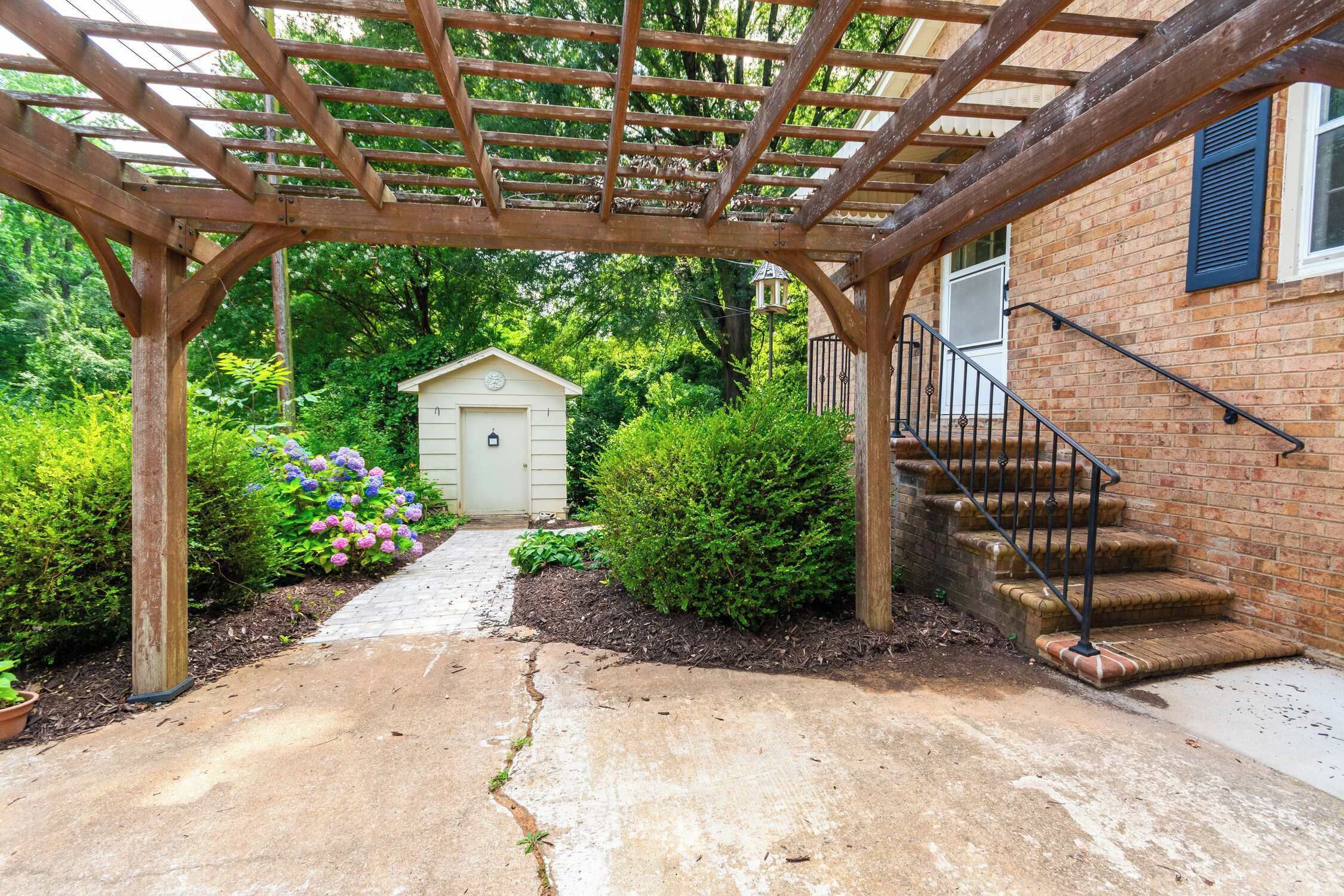 Une pergola en bois, un bâtiment en briques avec un escalier et un petit abri de jardin.
