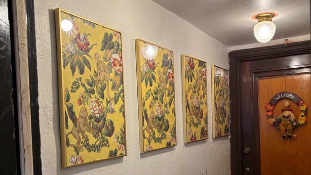 Ein Flur mit floralen Wandbildern, einem kleinen Tisch mit einer Vase und einer Tür mit einer Willkommensschild.