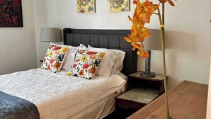 Ein Schlafzimmer mit einem Bett, Kissen, einem Nachttisch, einer Lampe und einer Zimmerpflanze.